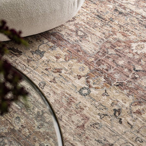 Close-up of a patterned rug with a beige ottoman and glass table in the foreground.