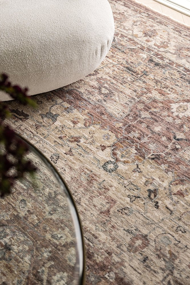 Close-up of a patterned rug with a beige ottoman and glass table in the foreground.